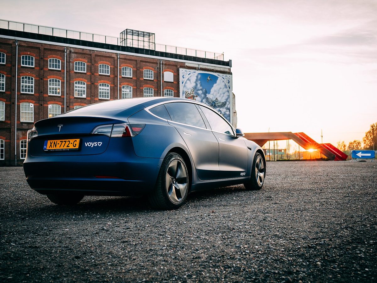 Blue wrapped Tesla Model 3 with company branding at sunset